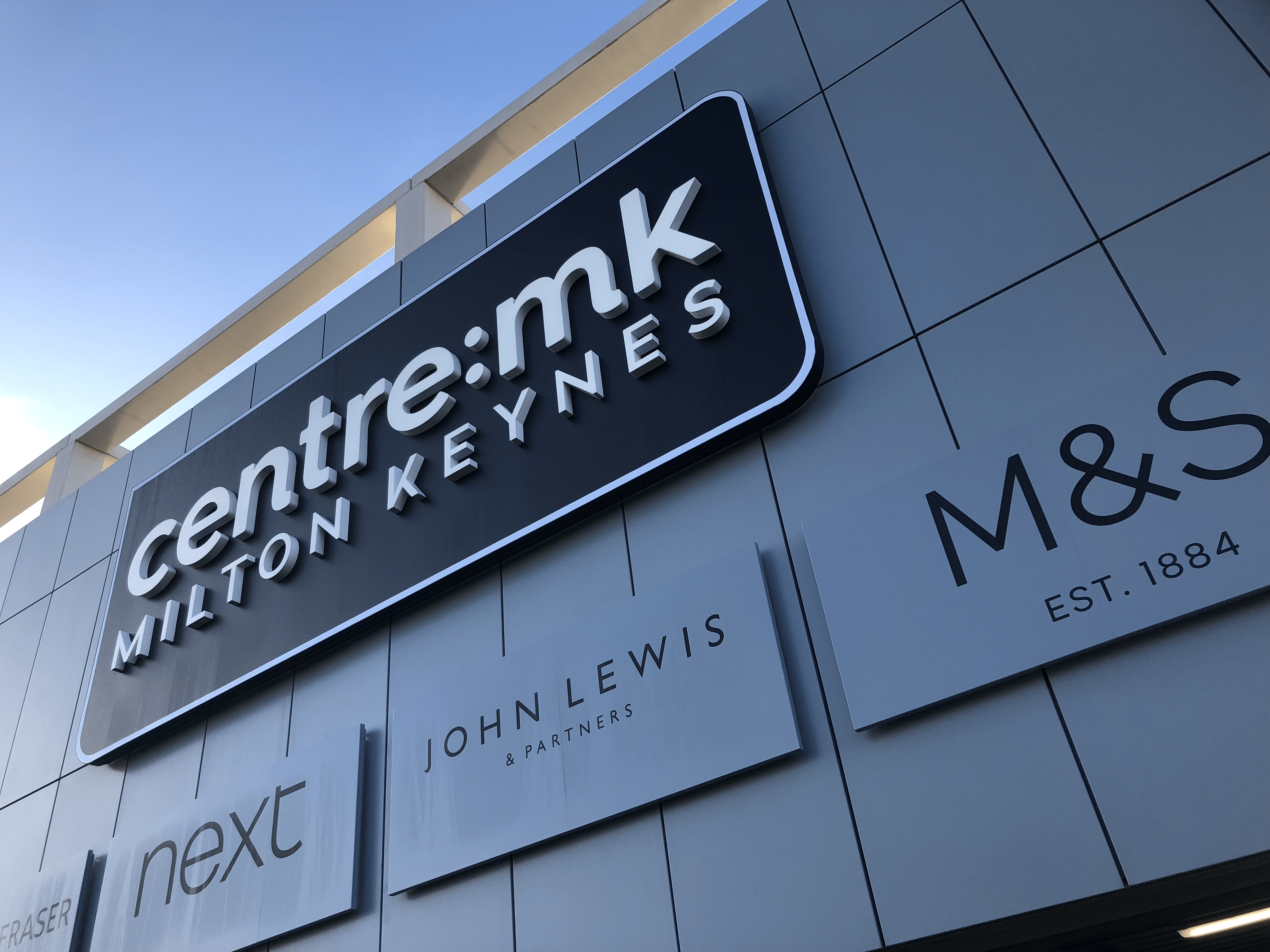 Five clothing retail shop signs on the wall on the exterior of a shopping centre after brand guidelines were followed in the design meeting process effectively.