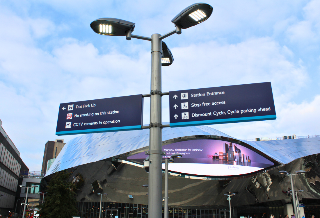 Directional wayfinding signage outside a UK train station, helping passengers navigate with clear instructions for station access, taxi pickup, and cycle parking.