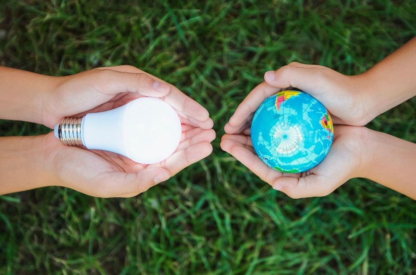 Two people holding a small ball of the earth and a lightbulb to symbolise energy saving and sustainable signage solutions 