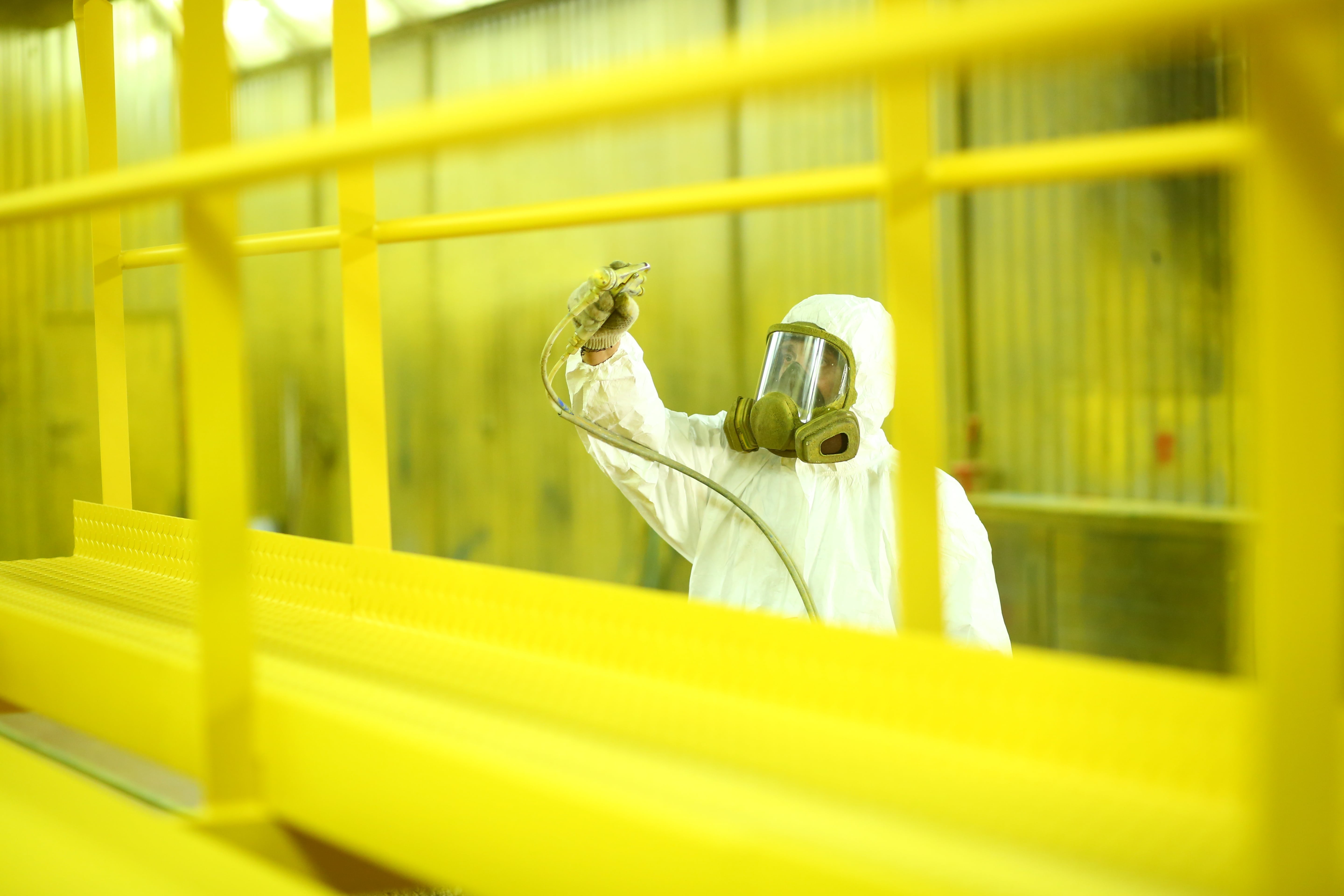 A man wearing a hazmat suit spray painting a sign as part of manufacturing process for signage creation and installation